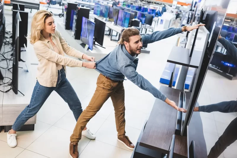 girlfriend-pulling-sad-boyfriend-with-tv-in-home-a-2024-11-11-07-00-46-utc Black Friday vs Cyber Monday 2025 electronics shopping — TVs and deals
